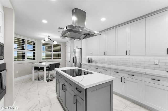 kitchen featuring light stone counters, island exhaust hood, stainless steel fridge, decorative backsplash, and black electric stovetop