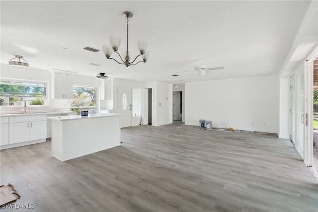 kitchen featuring light wood-type flooring, ceiling fan with notable chandelier, sink, pendant lighting, and white cabinets