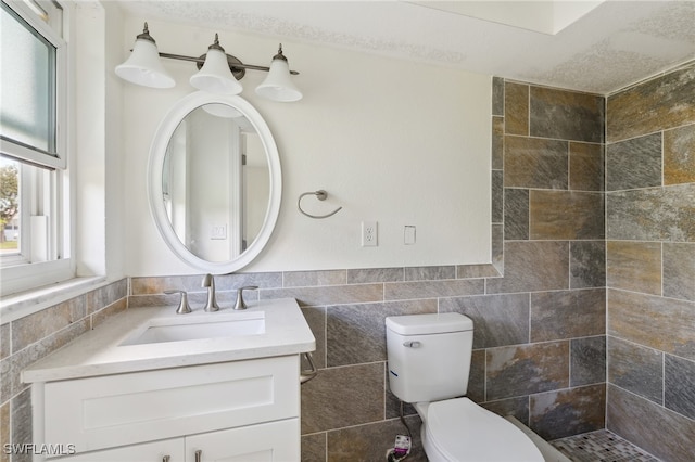 bathroom featuring a textured ceiling, vanity, toilet, and tile walls