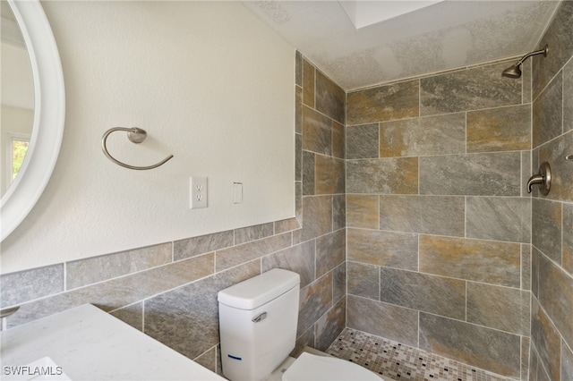 bathroom featuring a tile shower, toilet, and tile walls