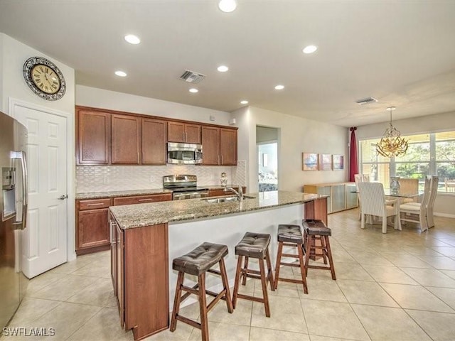 kitchen with sink, an inviting chandelier, an island with sink, decorative light fixtures, and appliances with stainless steel finishes