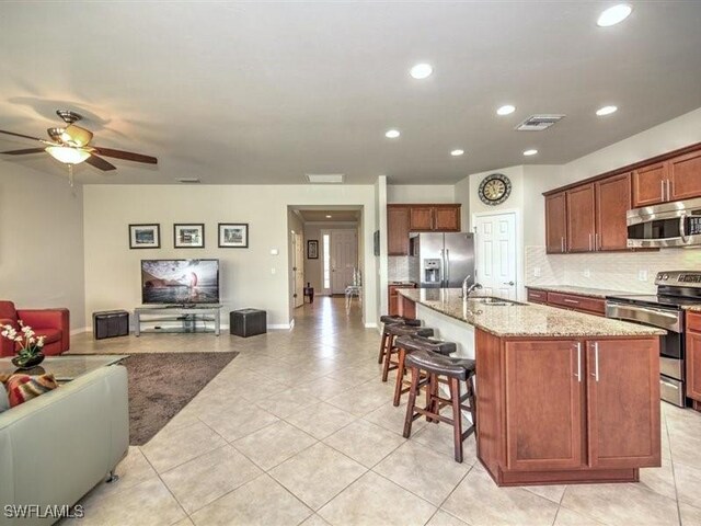 kitchen with a kitchen island with sink, a breakfast bar area, decorative backsplash, light stone counters, and stainless steel appliances