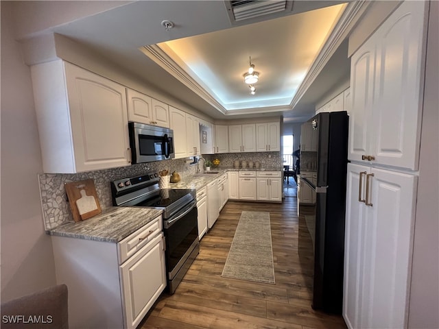 kitchen featuring a raised ceiling, white cabinets, dark wood-type flooring, and appliances with stainless steel finishes