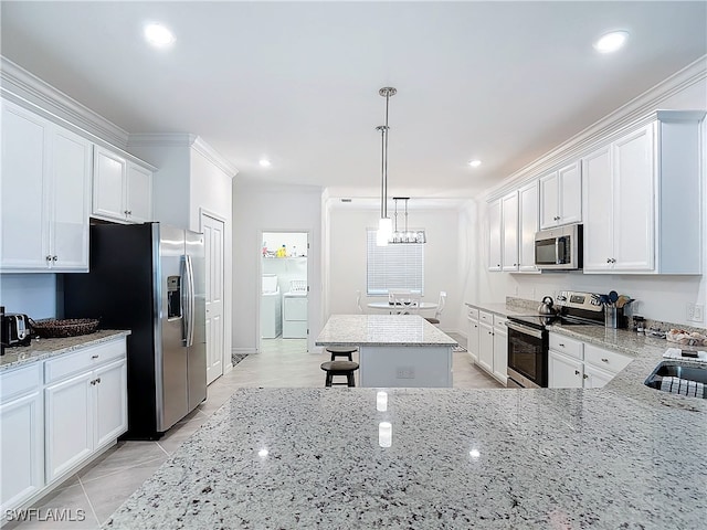 kitchen with washer and dryer, decorative light fixtures, a kitchen island, light stone counters, and stainless steel appliances