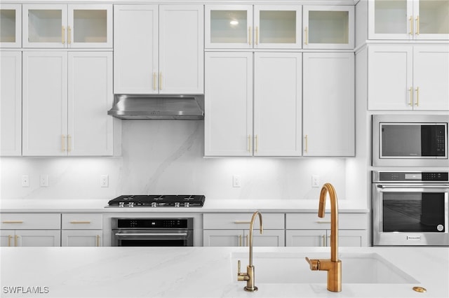 kitchen with sink, appliances with stainless steel finishes, light stone counters, white cabinetry, and extractor fan