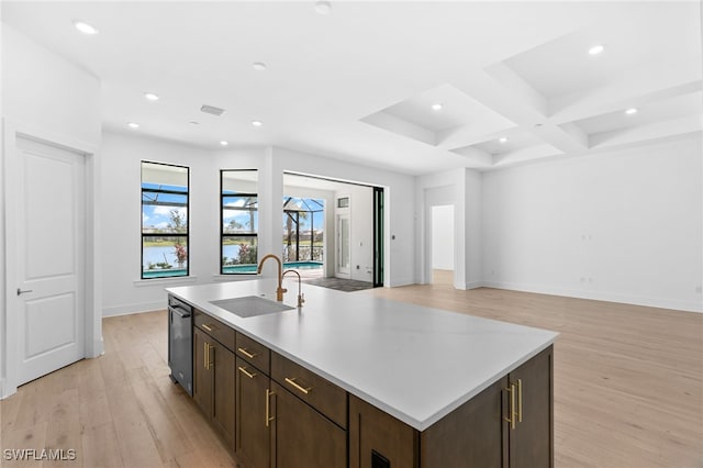 kitchen with light wood-type flooring, coffered ceiling, sink, beam ceiling, and a center island with sink