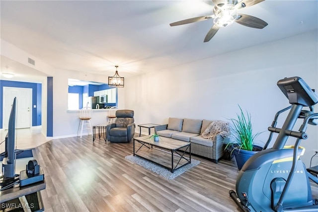 living area with ceiling fan with notable chandelier, wood finished floors, visible vents, and baseboards