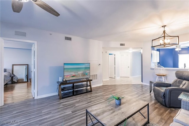 living area with ceiling fan with notable chandelier, visible vents, and wood finished floors