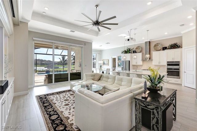 living room with ceiling fan, a tray ceiling, ornamental molding, and sink