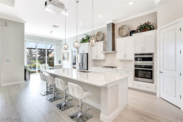 kitchen featuring pendant lighting, a breakfast bar, a large island with sink, white cabinets, and wall chimney range hood