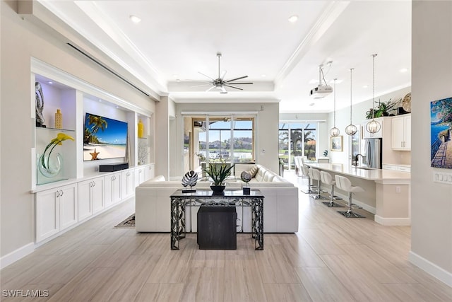 living room featuring a raised ceiling, ceiling fan, crown molding, and sink