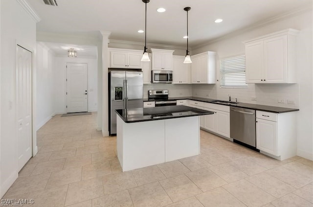 kitchen with appliances with stainless steel finishes, ornamental molding, pendant lighting, white cabinets, and a center island