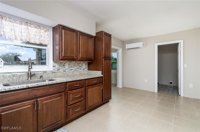 kitchen featuring light stone countertops, sink, a wall unit AC, backsplash, and light tile patterned floors