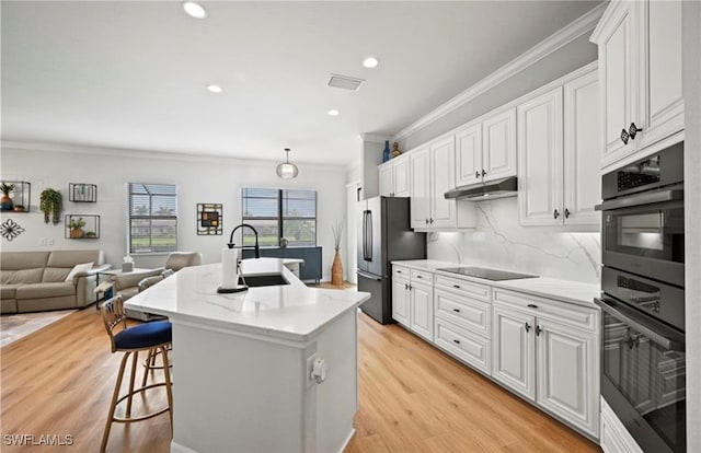 kitchen with ornamental molding, an island with sink, appliances with stainless steel finishes, light hardwood / wood-style floors, and white cabinetry