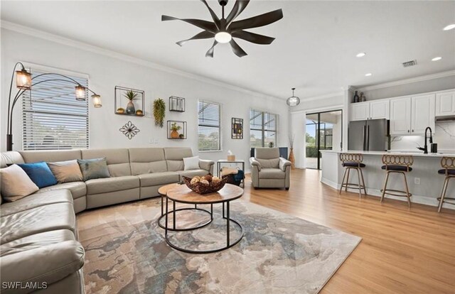 living room with ceiling fan, sink, light wood-type flooring, and crown molding