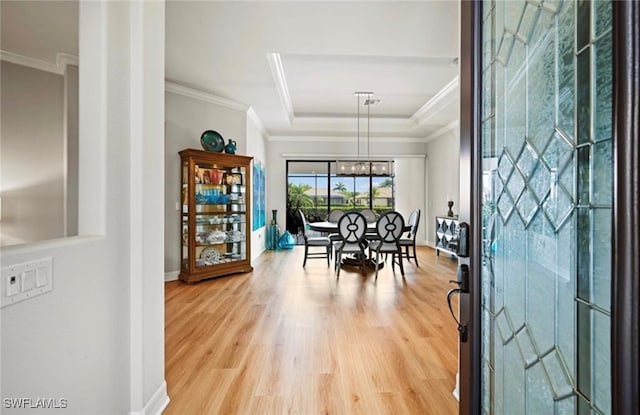 dining room with a tray ceiling, crown molding, a chandelier, and light wood-type flooring