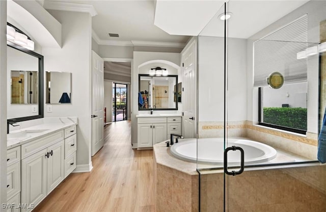 bathroom featuring vanity, wood-type flooring, crown molding, and tiled bath