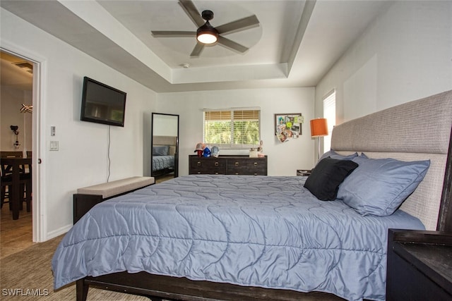 carpeted bedroom with ceiling fan and a tray ceiling