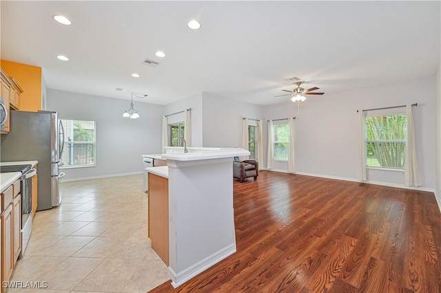 kitchen with stainless steel range with electric stovetop, ceiling fan with notable chandelier, a kitchen island with sink, light hardwood / wood-style flooring, and hanging light fixtures