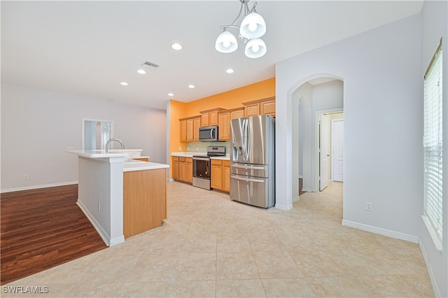 kitchen with appliances with stainless steel finishes, a kitchen island with sink, light hardwood / wood-style flooring, a chandelier, and hanging light fixtures