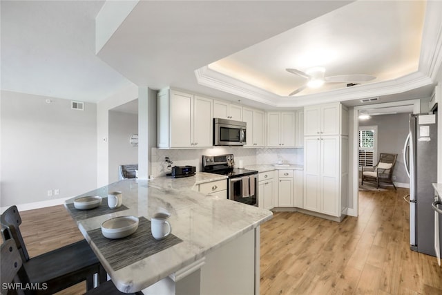 kitchen with stainless steel appliances, kitchen peninsula, a tray ceiling, white cabinets, and light wood-type flooring