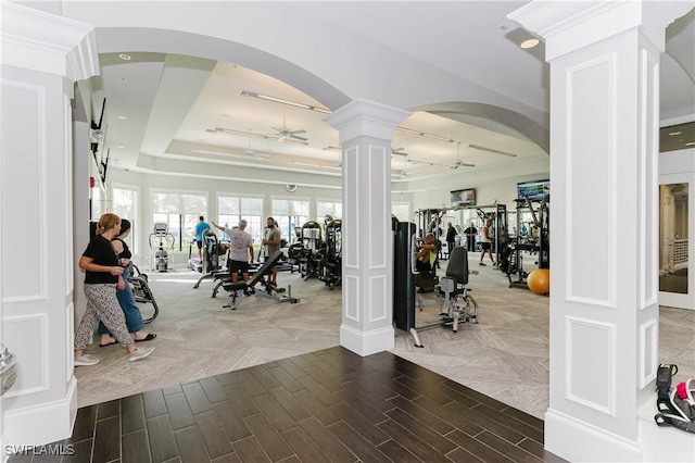 gym with ceiling fan, a raised ceiling, and ornate columns