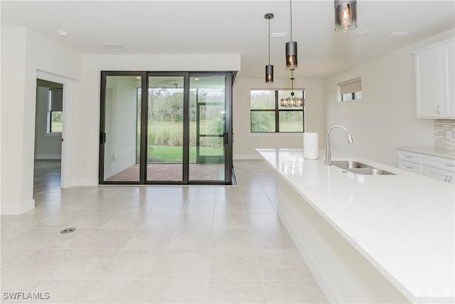 kitchen featuring white cabinetry, sink, decorative light fixtures, and light stone countertops