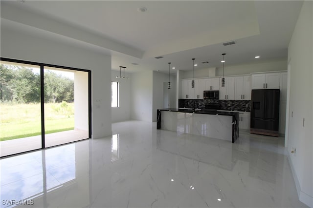 kitchen featuring decorative backsplash, black fridge with ice dispenser, a raised ceiling, white cabinetry, and hanging light fixtures