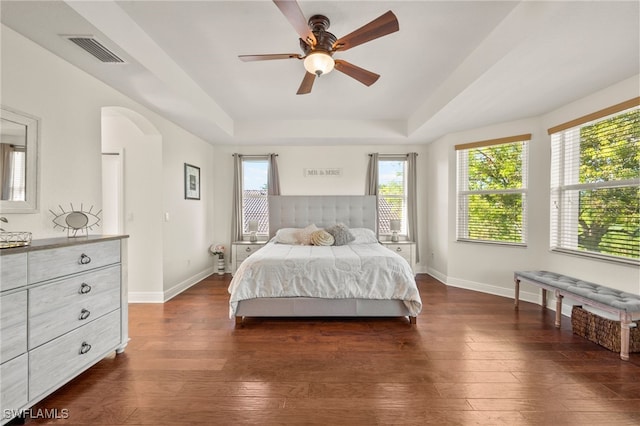 bedroom featuring a raised ceiling, multiple windows, ceiling fan, and dark hardwood / wood-style floors