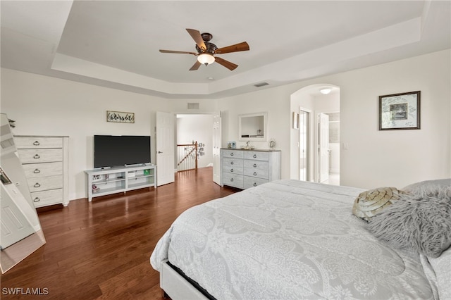 bedroom featuring ceiling fan, dark hardwood / wood-style floors, a raised ceiling, and ensuite bathroom