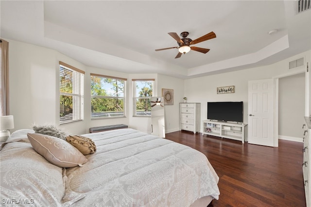 bedroom with a tray ceiling, ceiling fan, and dark wood-type flooring