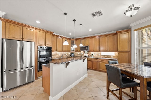 kitchen featuring hanging light fixtures, dark stone counters, a center island with sink, appliances with stainless steel finishes, and ornamental molding