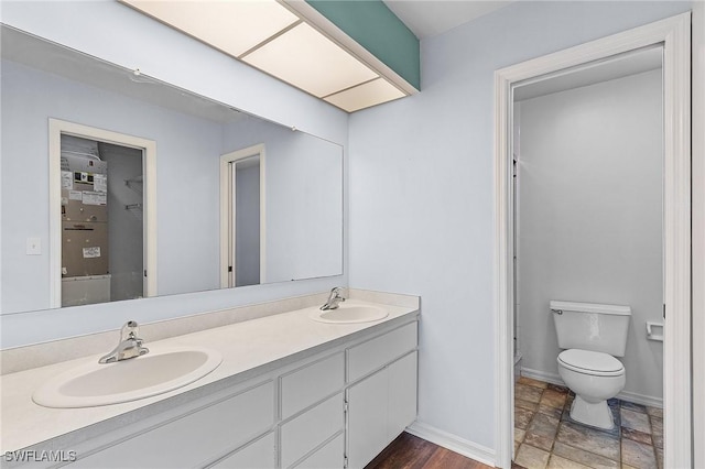 bathroom featuring baseboards, a sink, toilet, and double vanity