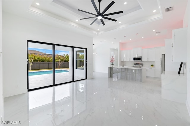 unfurnished living room with a raised ceiling, ceiling fan, and sink