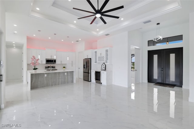 kitchen featuring white cabinetry, a spacious island, decorative light fixtures, a tray ceiling, and appliances with stainless steel finishes