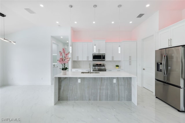 kitchen with appliances with stainless steel finishes, white cabinetry, hanging light fixtures, and a kitchen island with sink