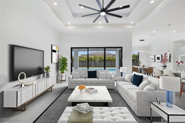 living room with a raised ceiling, ceiling fan, crown molding, and a high ceiling