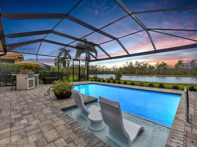 pool at dusk featuring a patio, a water view, glass enclosure, and exterior kitchen