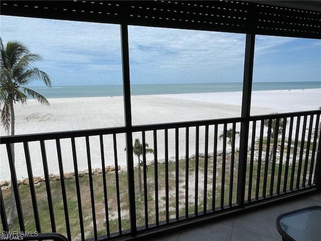 sunroom featuring plenty of natural light, a water view, and a view of the beach