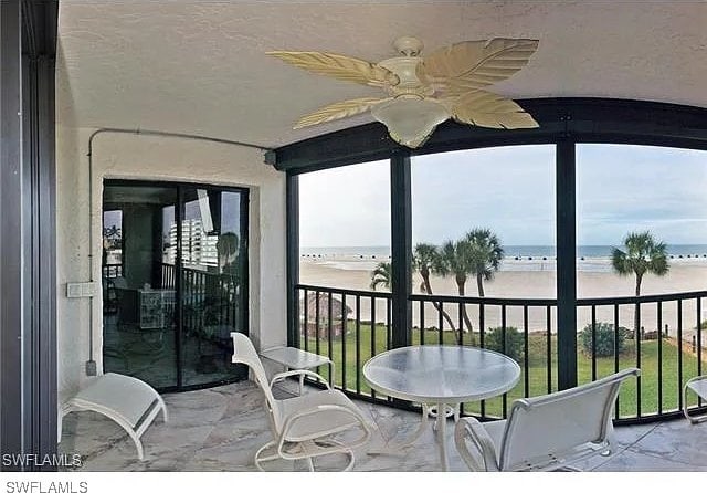 sunroom with ceiling fan, a healthy amount of sunlight, a water view, and a beach view