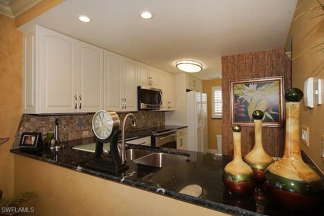 kitchen featuring white cabinets, stainless steel appliances, kitchen peninsula, and dark stone counters