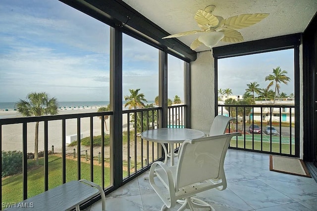 sunroom / solarium with ceiling fan, a water view, a wealth of natural light, and a view of the beach