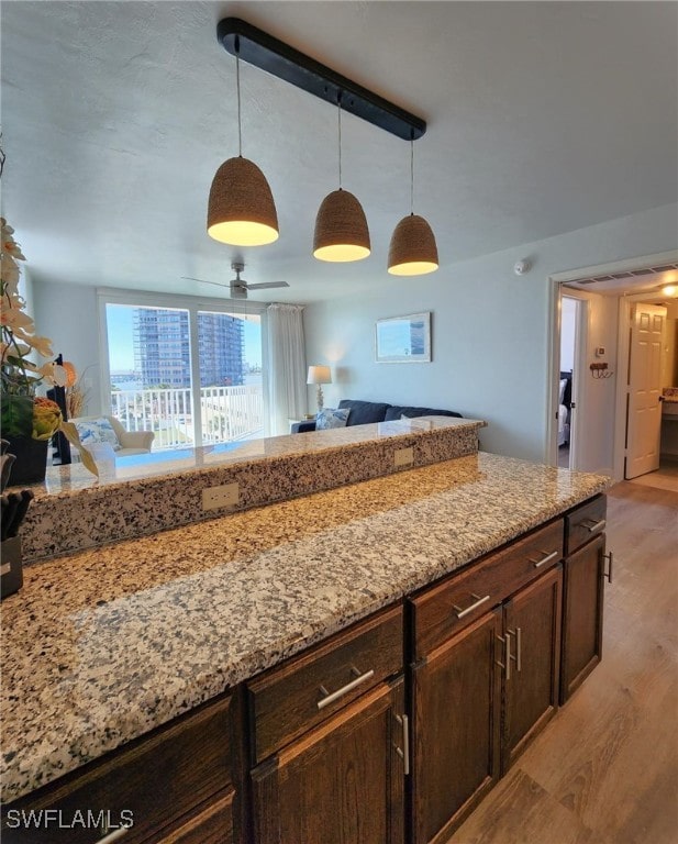 kitchen with pendant lighting, light hardwood / wood-style flooring, ceiling fan, dark brown cabinets, and light stone counters