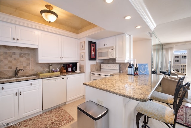 kitchen with a kitchen bar, decorative backsplash, white cabinetry, and white appliances