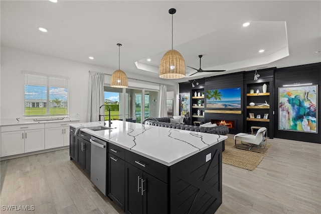 kitchen with a raised ceiling, a kitchen island with sink, stainless steel dishwasher, and sink