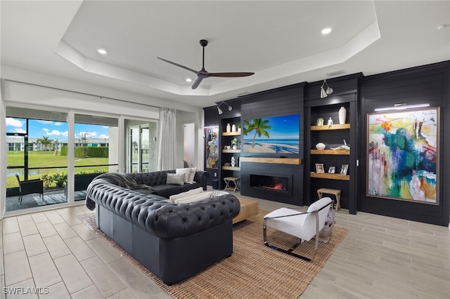 living room featuring light wood-type flooring, a tray ceiling, and ceiling fan