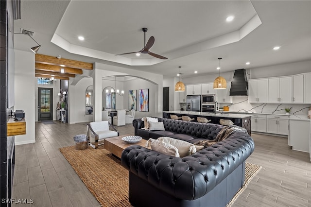 living room featuring a raised ceiling, ceiling fan with notable chandelier, and light wood-type flooring