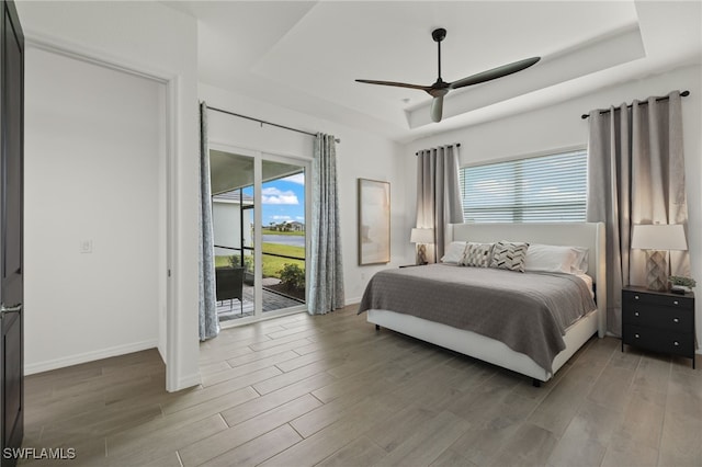 bedroom with access to outside, ceiling fan, a tray ceiling, and hardwood / wood-style flooring