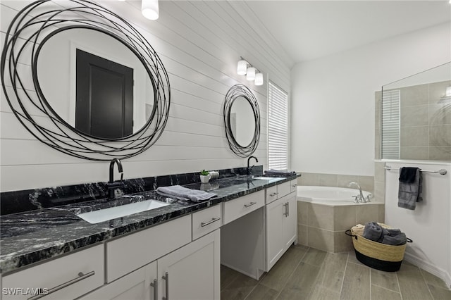 bathroom with tiled tub, vanity, and wood-type flooring