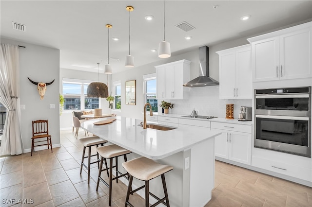 kitchen featuring pendant lighting, wall chimney exhaust hood, sink, and double oven